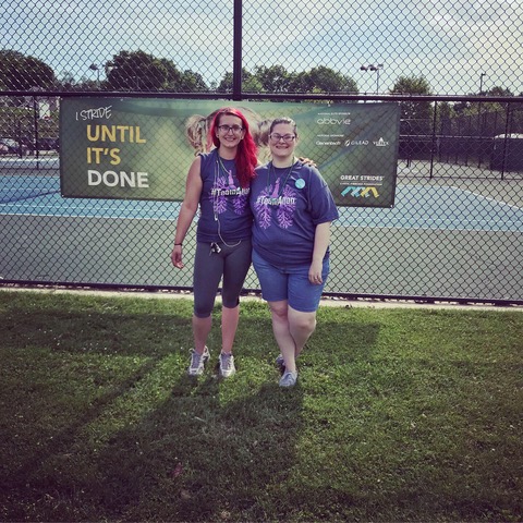 Two friends standing in front of a banner in custom shirts at a fundraiser walk