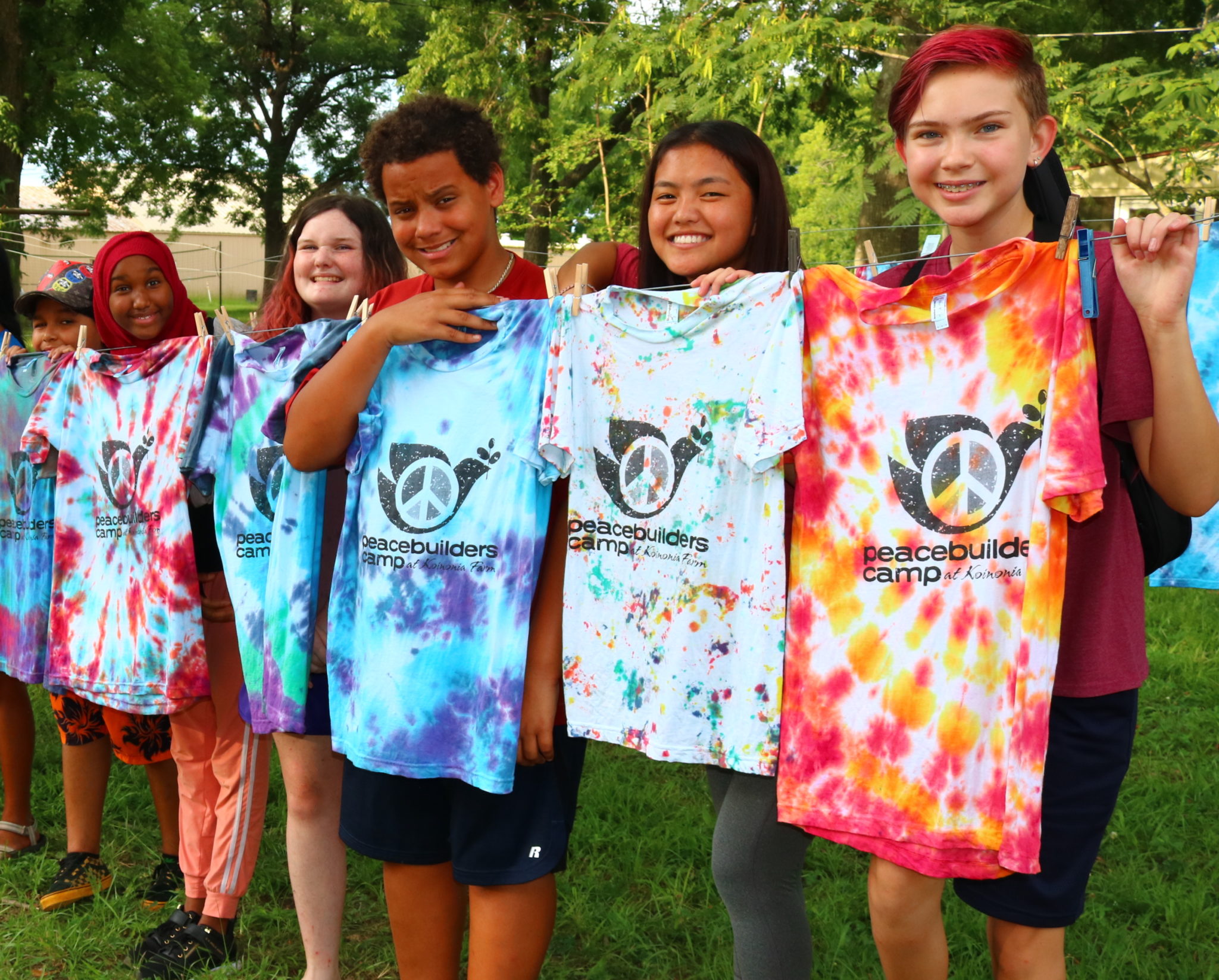 Campers hold up their custom tie-dyed Peacebuilders Camp shirts.