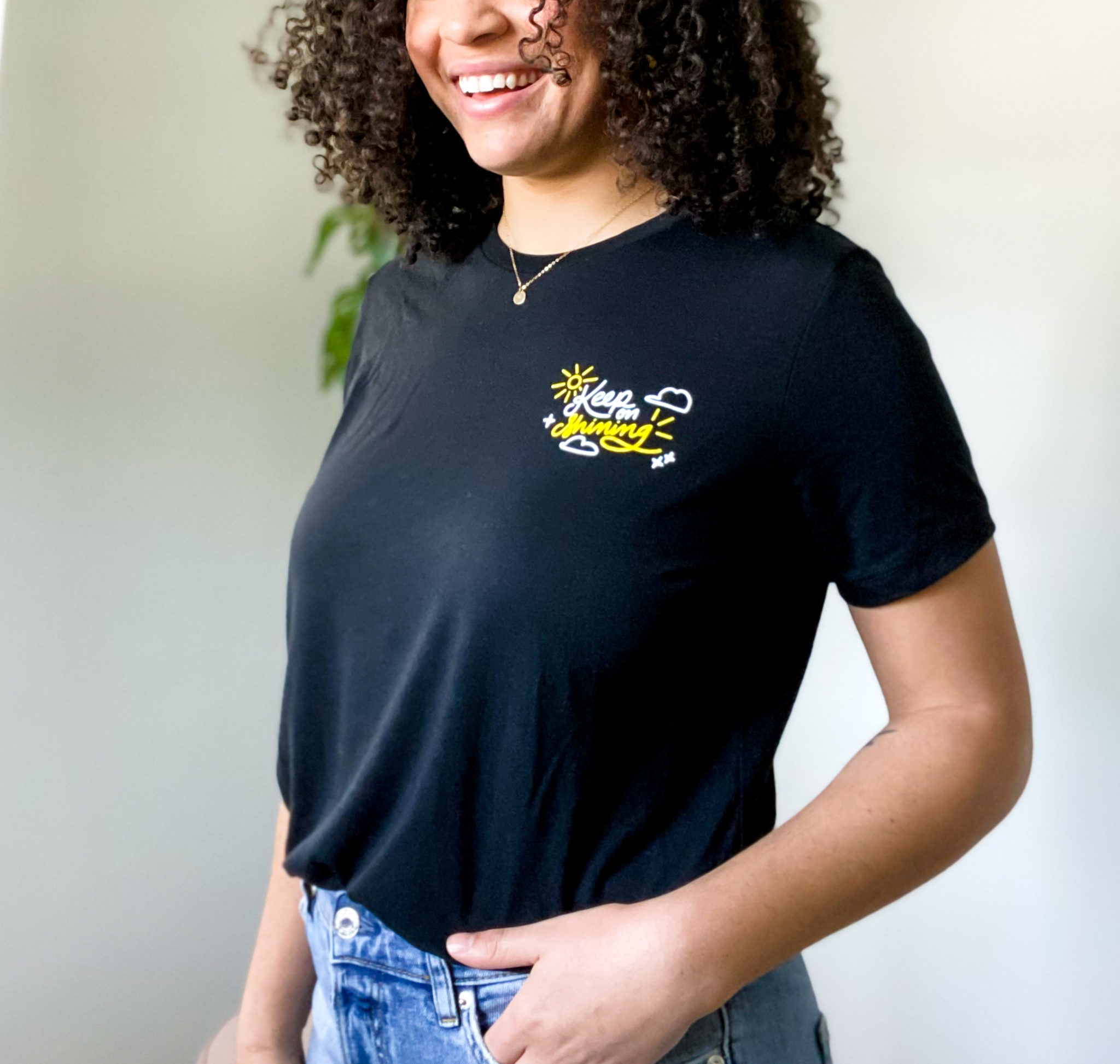 a woman smiles wearing a black custom t-shirt with a yellow and white design that says Keep Smiling with a sun and clouds
