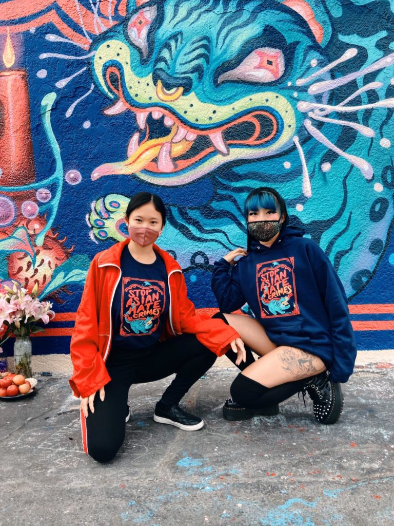 Lauren YS and a friend posing in front of the Stop Asian Hate Crimes mural in matching Stop Asian Hate Crimes apparel