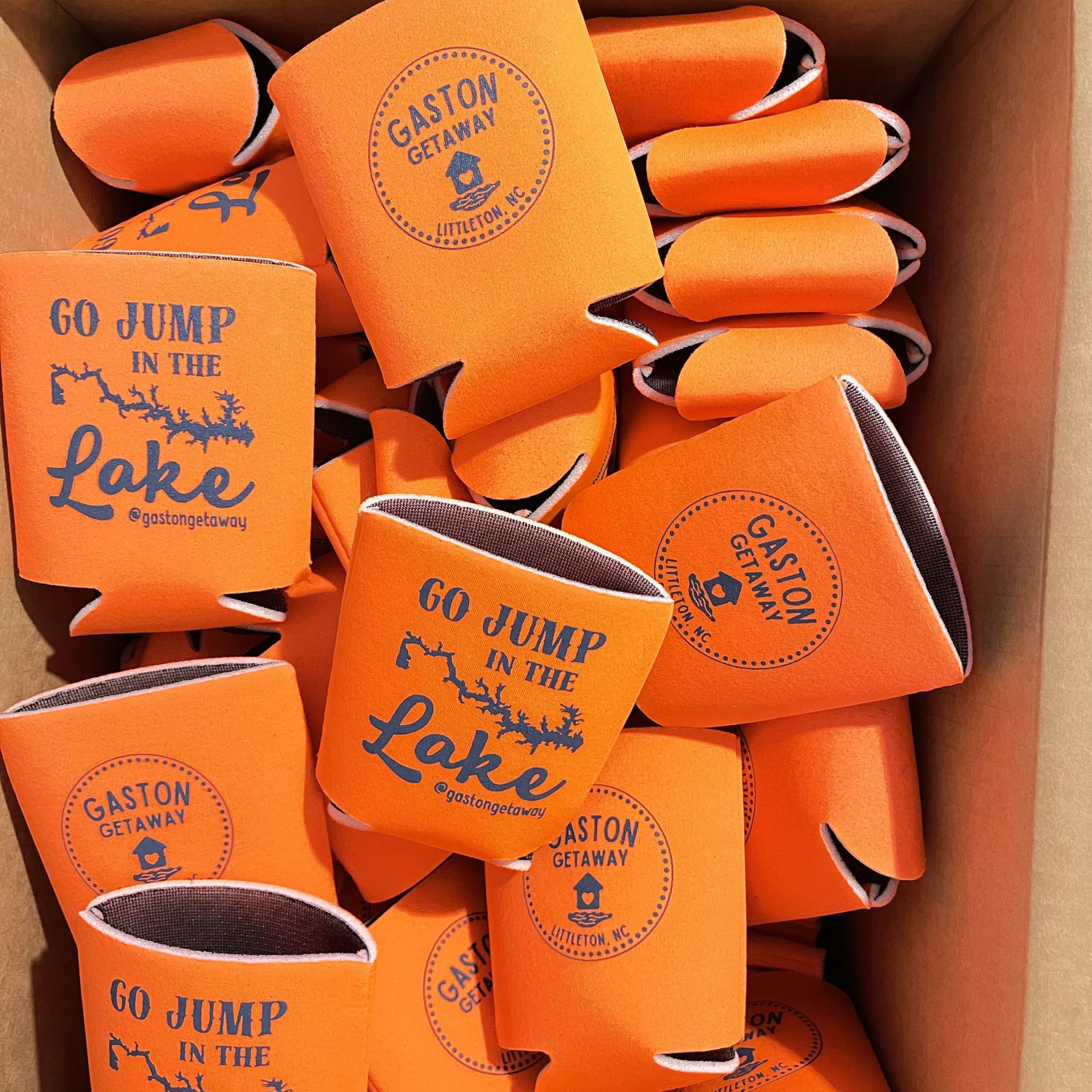 a box full of custom can coolers that say "go jump in the lake" and "gaston getaway"