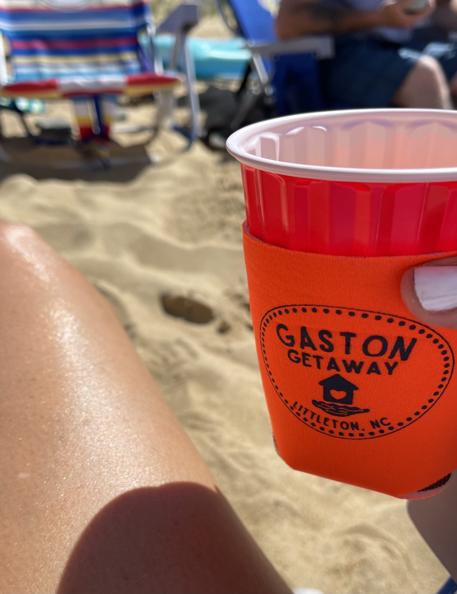 a person holds a plastic cup with a custom can cooler on it that says "Gaston Getaway"