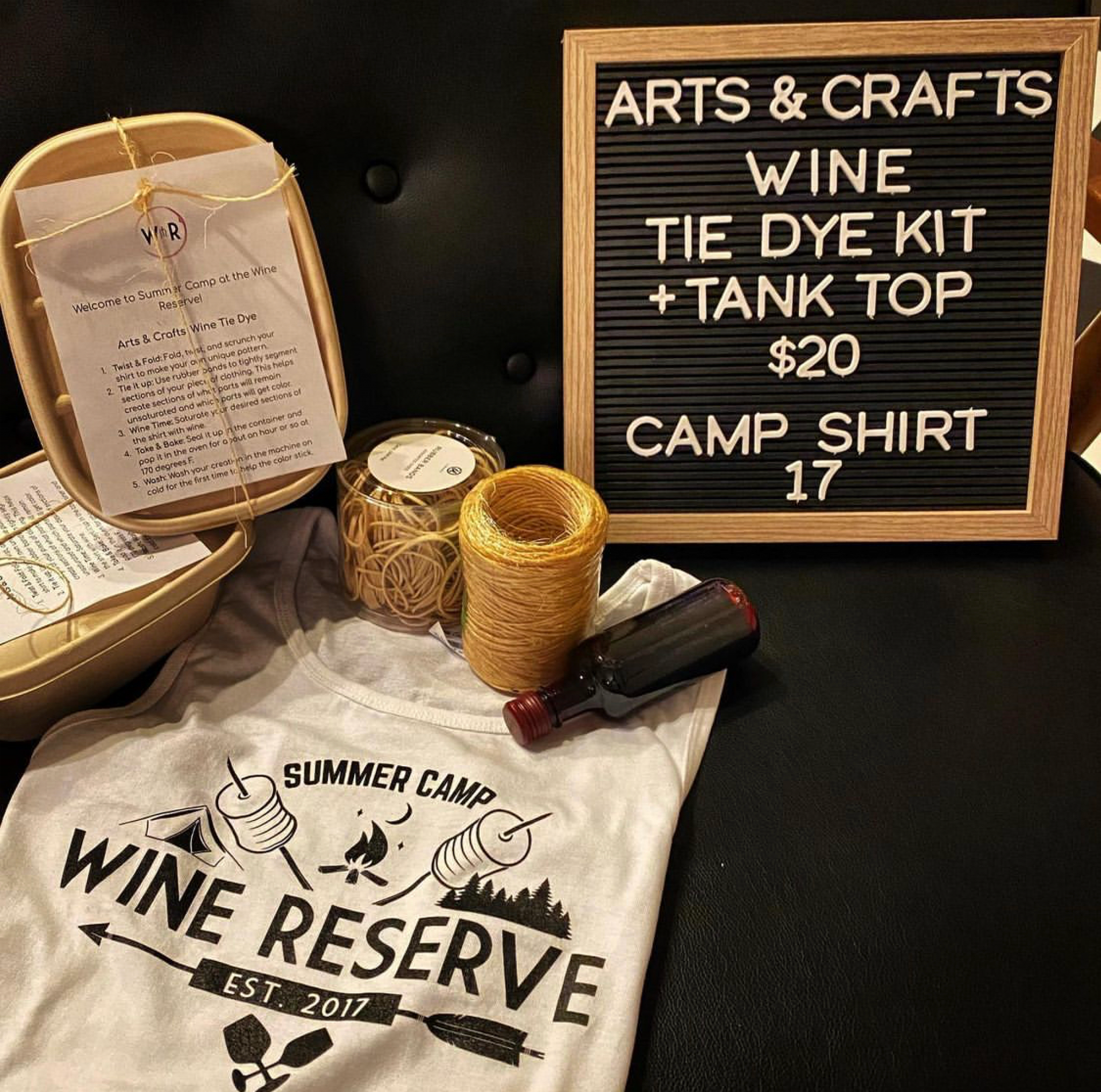 a custom t-shirt that says "Summer Cam Wine Reserve Est. 2017" along with a sign that says "Arts & Crafts Wine Tie Dye Kit + Tank Top $20 Camp Shirt 17". There are tie dye kit parts arranged around the shirt. 