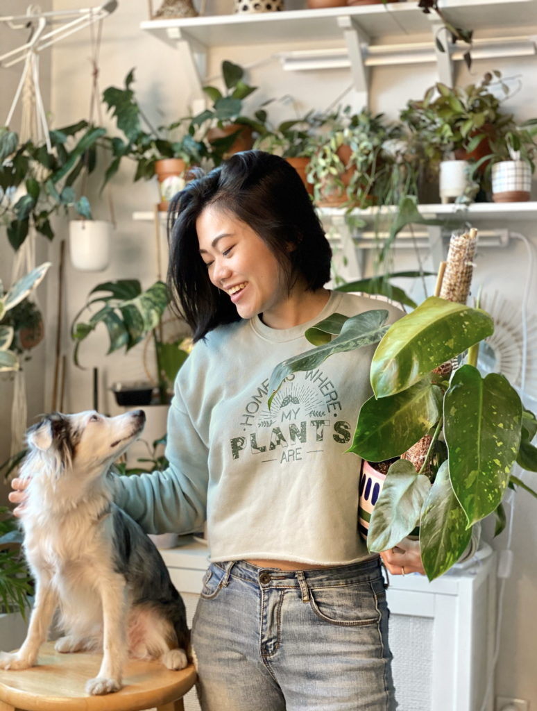 A woman in a cropped sweatshirt with Home Is Where My Plants Are pets a dog