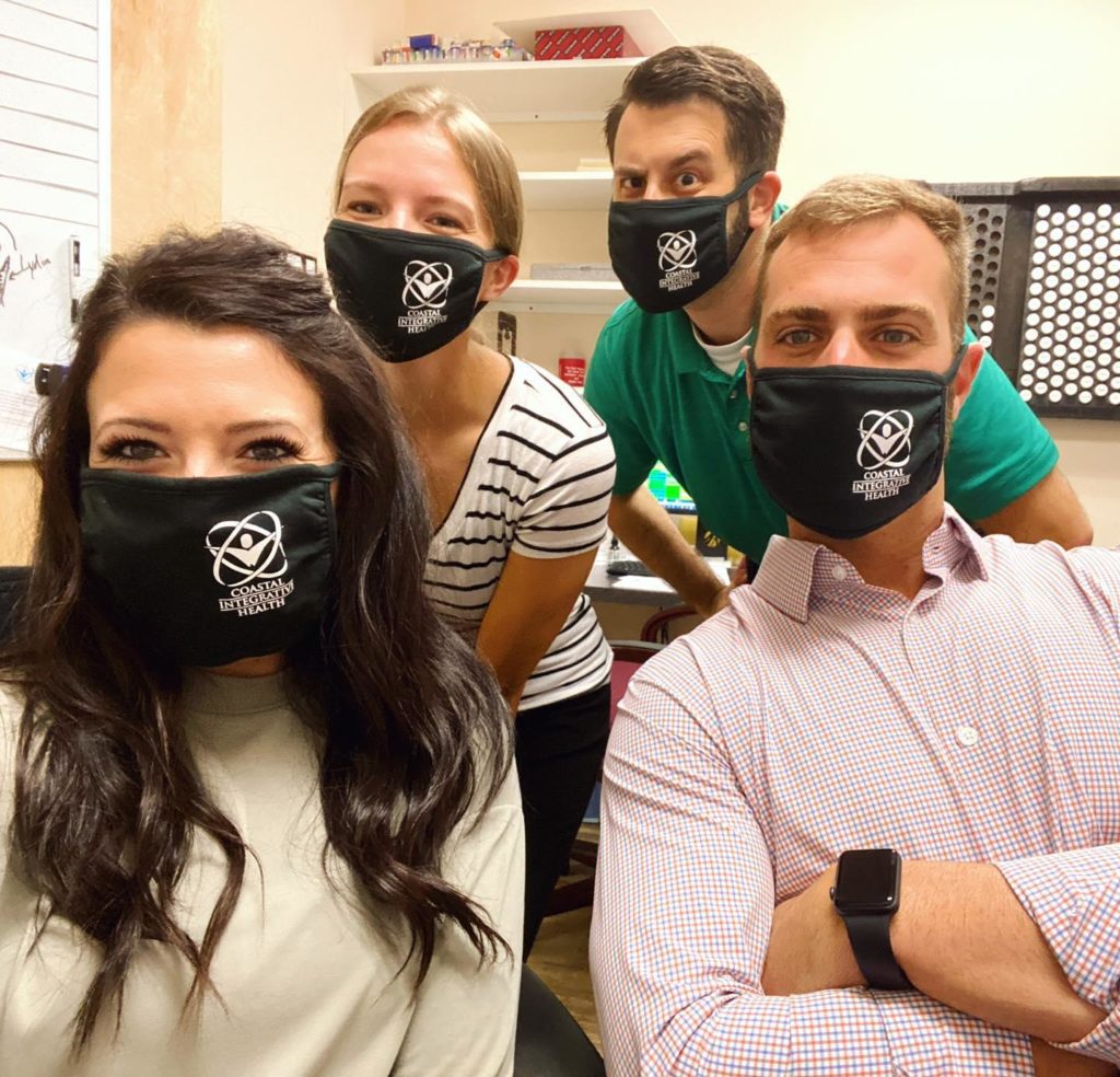 Two men and two women in a professional setting wearing facemasks with Coastal Integrative Health printed on the masks