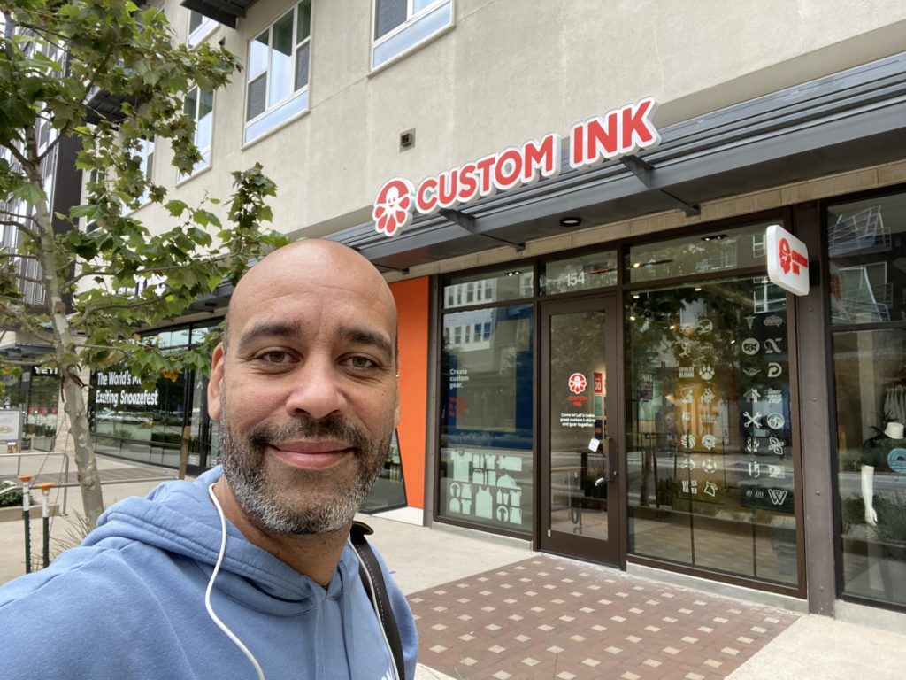 Custom Ink employee in front of a Custom Ink storefront.
