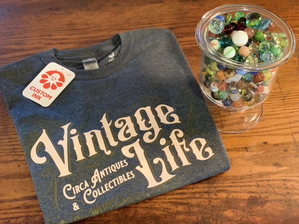 Jar of antique marbles next to folded shirt with "Vintage Life" printed on it.