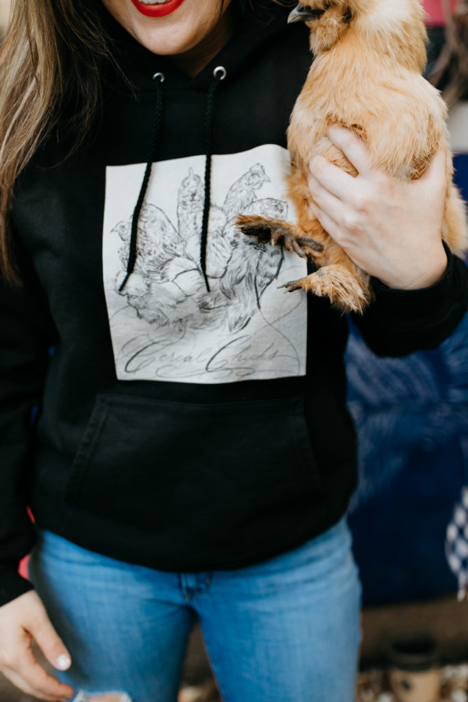 Closeup of woman holding a chicken and wearing a hoodie with Cereal Chicks art