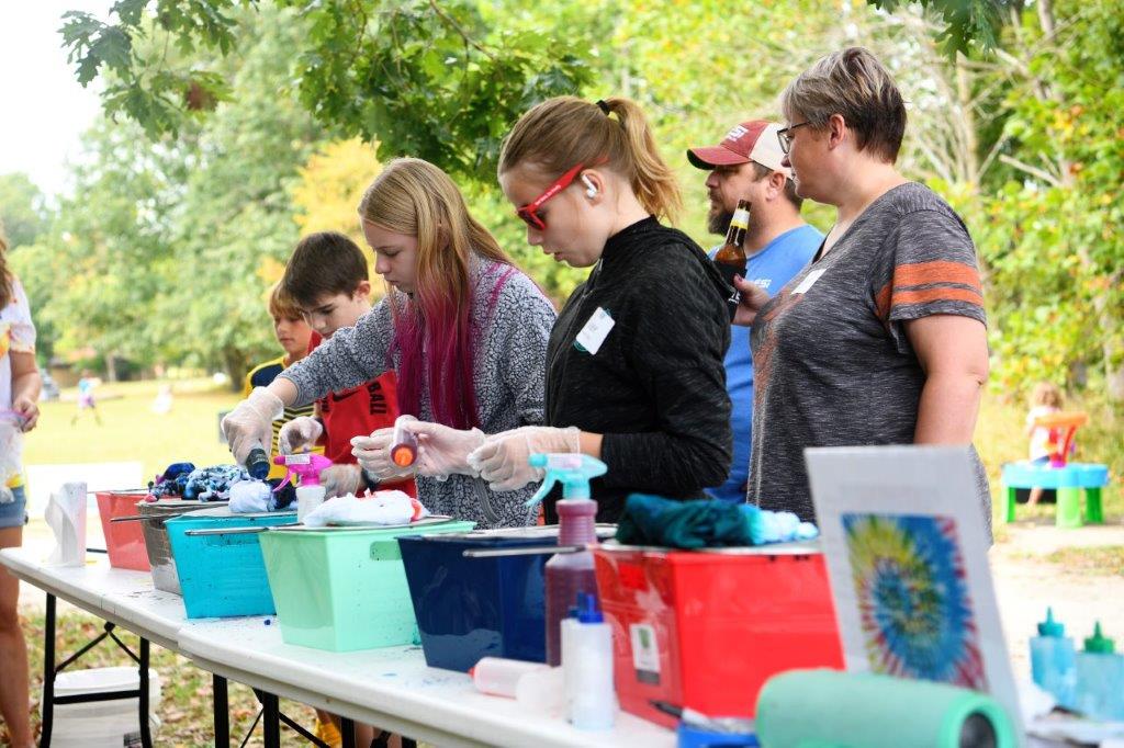 A line of adults and children adding dye to receptacles, preparing shirts to be dyed