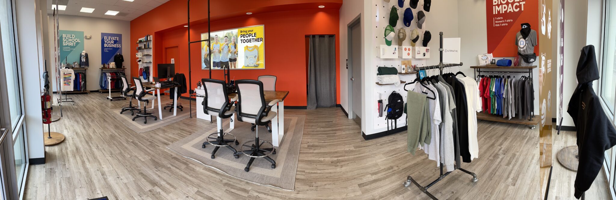 The interior of a Custom Ink showroom, with stations comprised of desks and chairs as well as a rack of products.